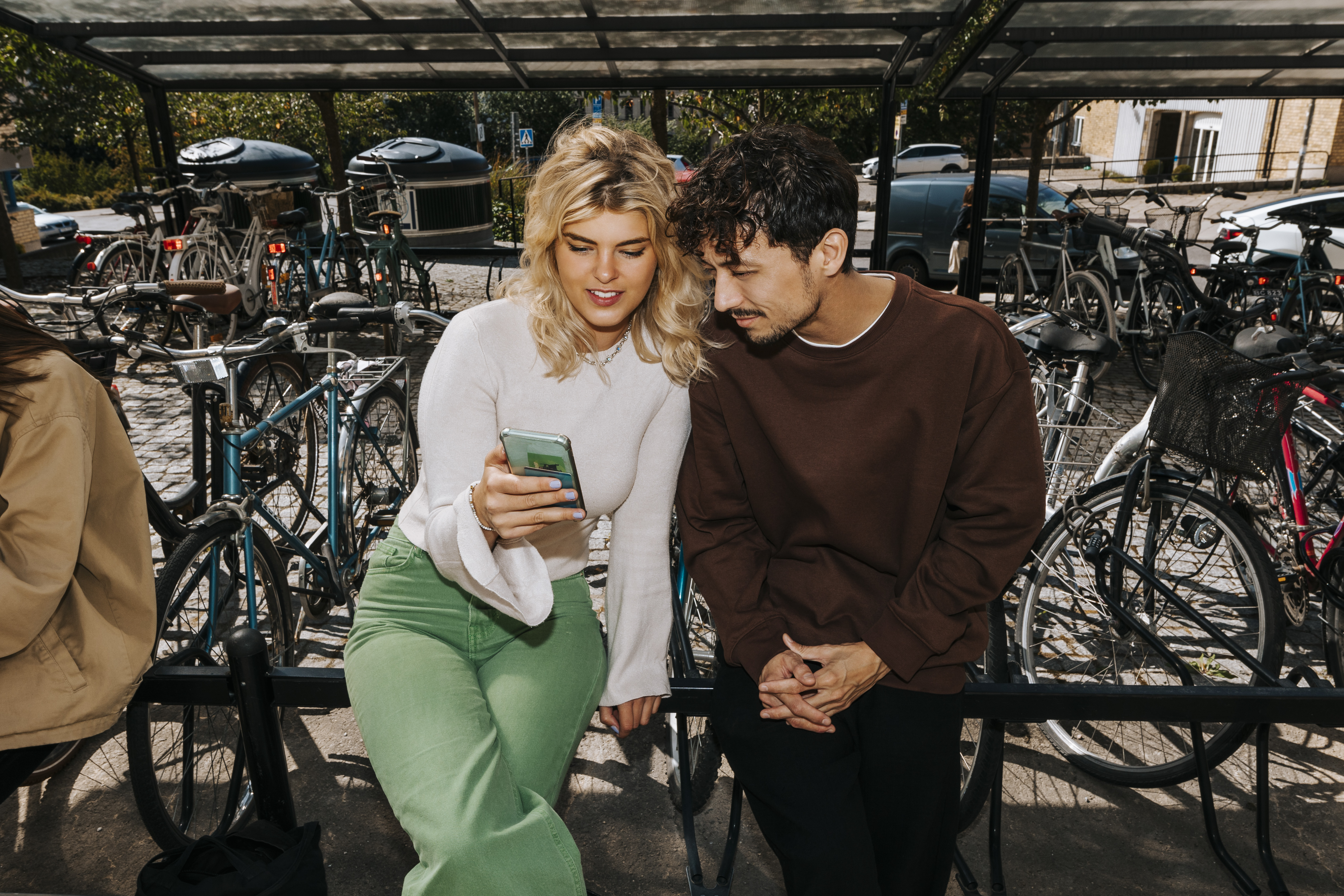 Tv&aring; personer sitter p&aring; ett cykelst&auml;ll och tittar p&aring; en mobil tillsammans och ler